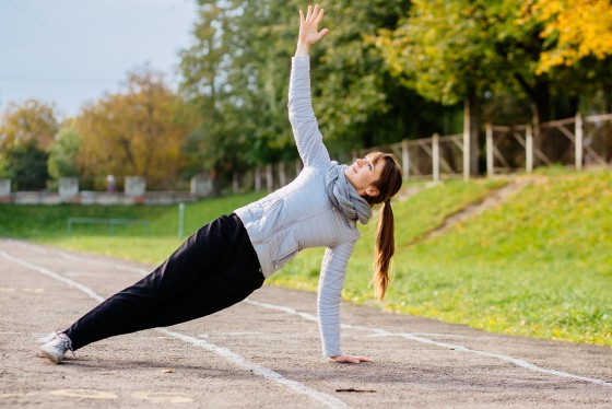 Young brunette sporty woman warming up - doing plank exercises in track of stadium. Autumn, fall and cold season concept.