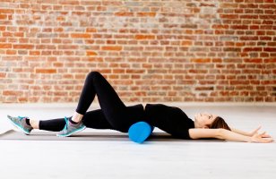 Young fitness woman in black sportswear doing stretching exercise with foam roller  in modern loft interior at gym. Sport, fitness, lifestyle and people concept